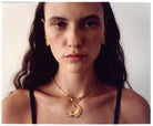 A close-up portrait of a model wearing an EFEK gold cat pendant necklace and gold earrings from the Cats of Istanbul collection.